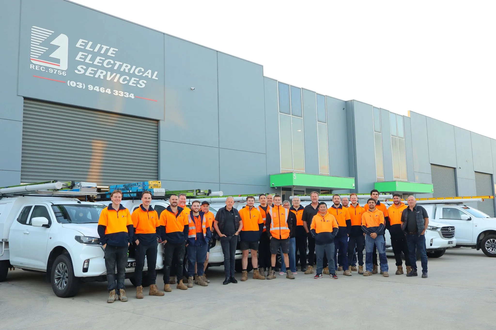 The Elite Electrical Services team standing in front of their headquarters with company vehicles